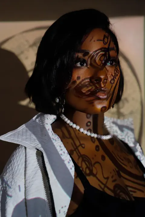 Efya in profile, patterned light across her face, pearls at her neck