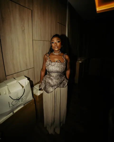 Efya in a silver dress in a dark corridor