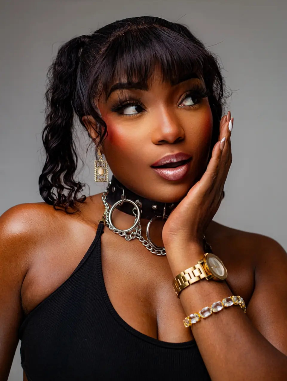 Efya in a black top, hand to cheek, gold watch