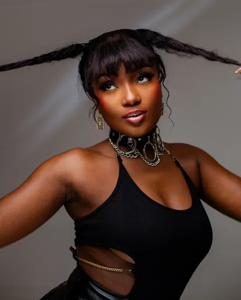 Efya in a black top, arms raised, gold jewellery