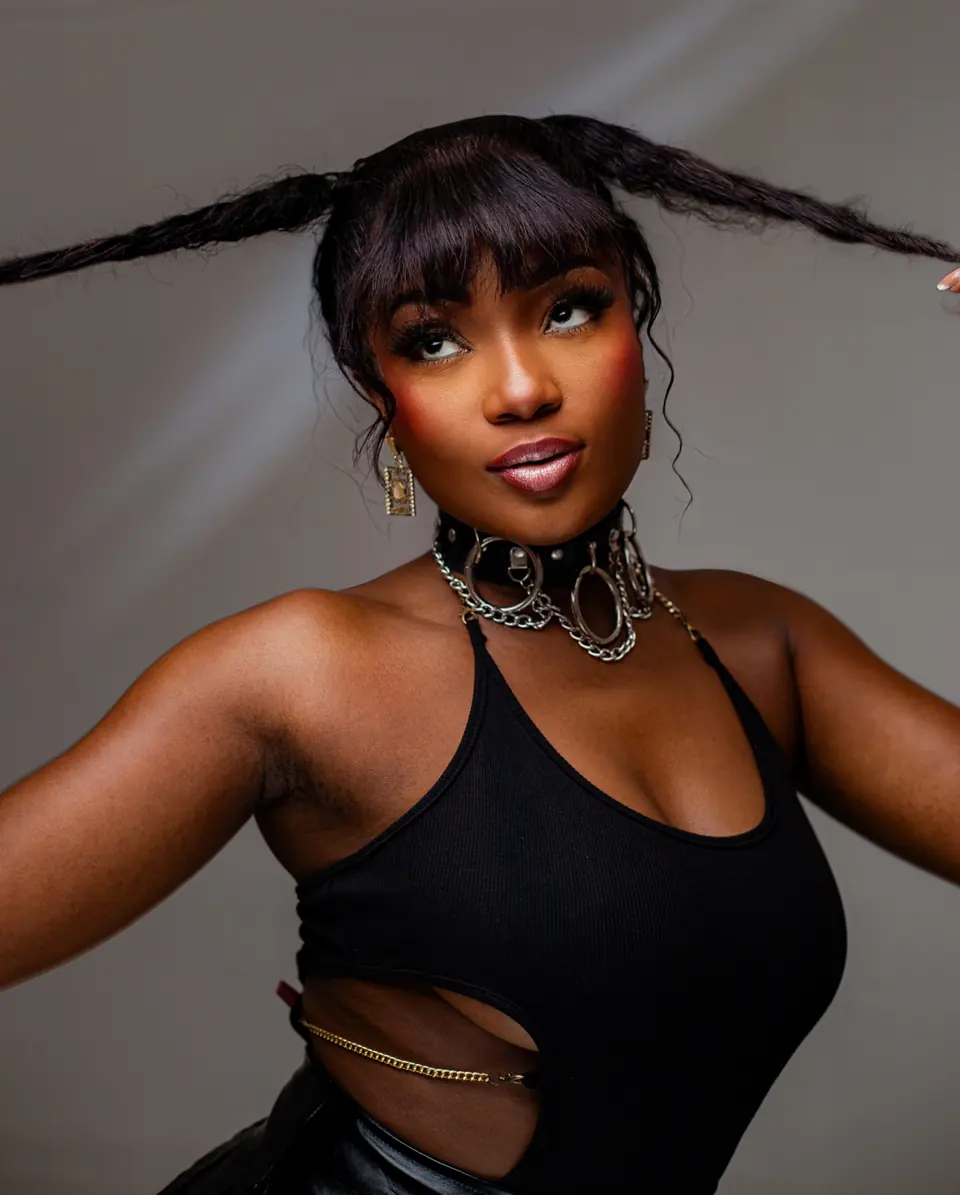 Efya in a black top, arms raised, gold jewellery